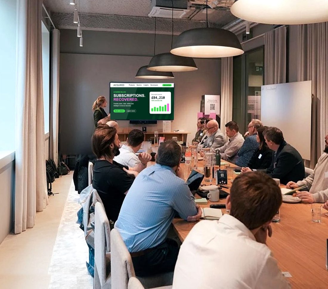 An Acquired team member presenting Acquired Billing on a wall screen to guests seated around a long meeting table